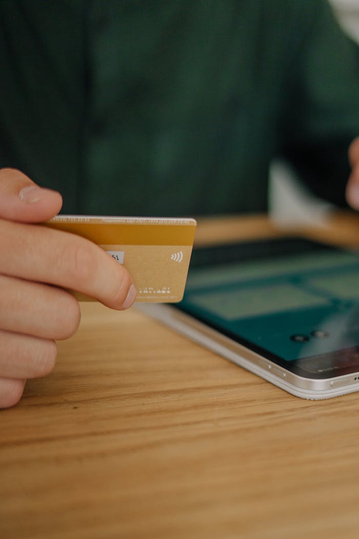 Person holding a credit card, making a contactless payment on a tablet indoors.